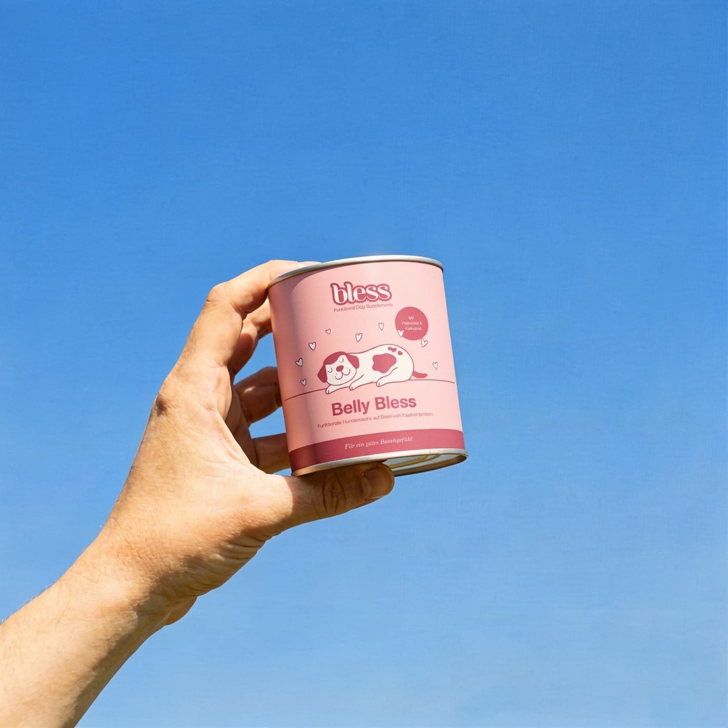 Hand hält eine Belly Bless Dose vor blauem Himmel